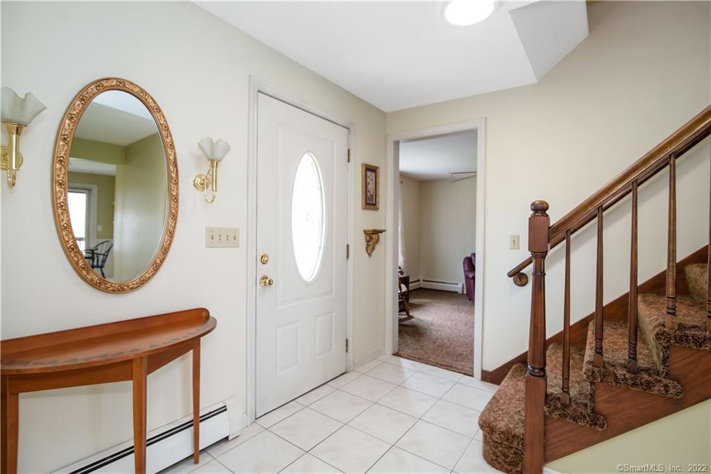 Entry foyer with tiled floor, oval-glass front door, wooden console table, and carpeted staircase.