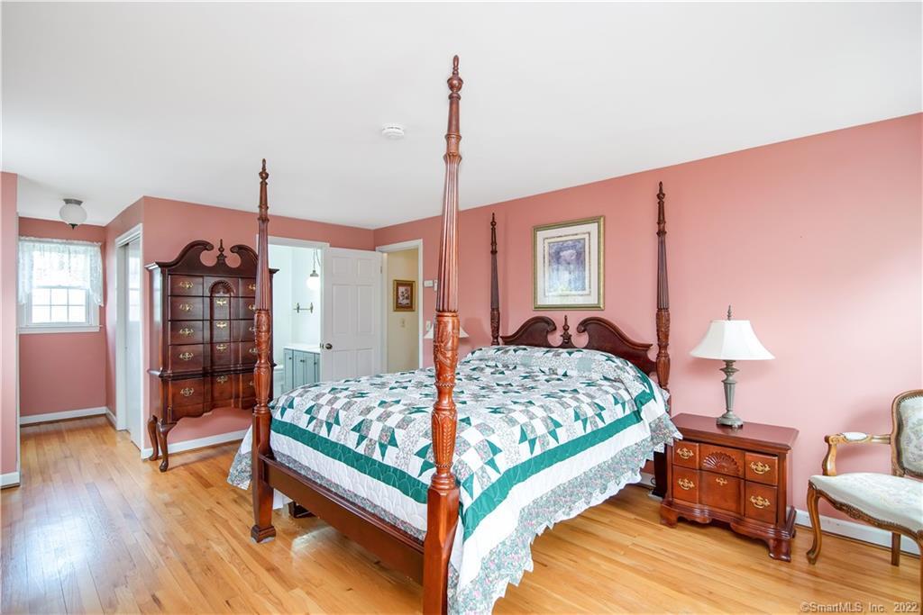 Bedroom with a four-poster bed, teal-and-white quilt, pink walls, and hardwood floors.