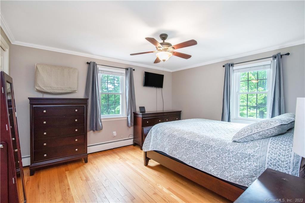Bedroom with hardwood floors, dark wood dressers, and two curtained windows.