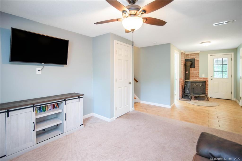 Living room with a wall-mounted TV, ceiling fan, and wood stove near a glass-paneled door.