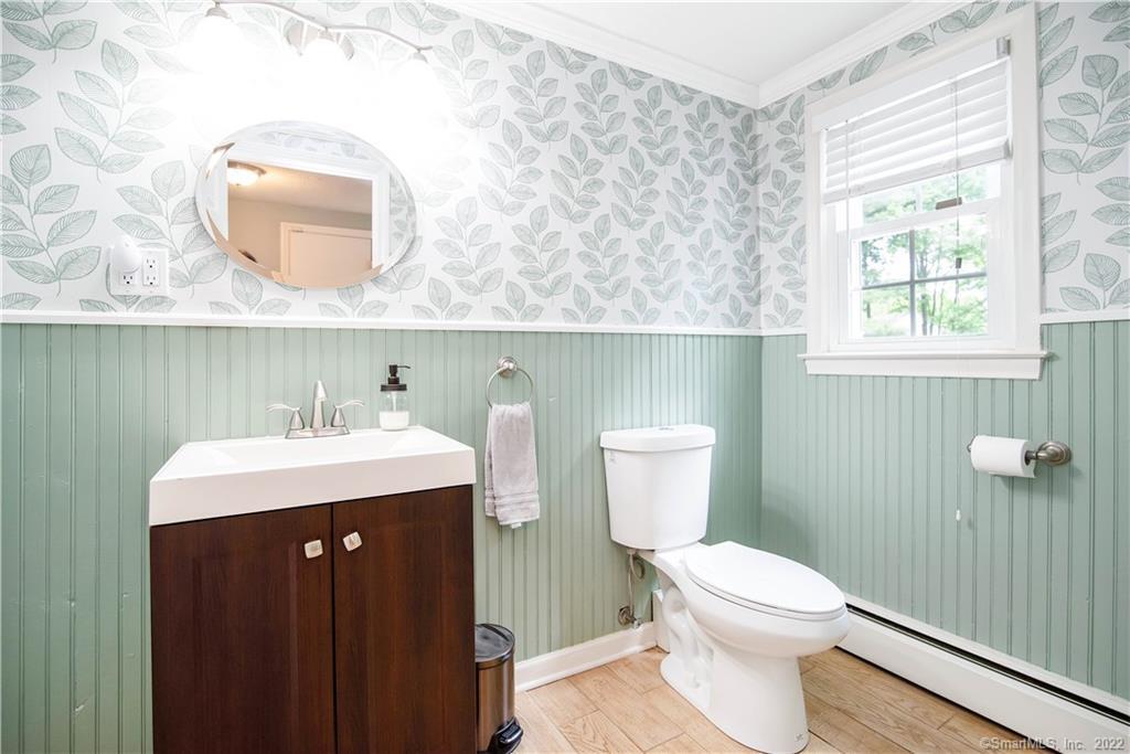 Bathroom with mint-green paneling, leafy wallpaper, a dark wood vanity, and a window with white blinds.