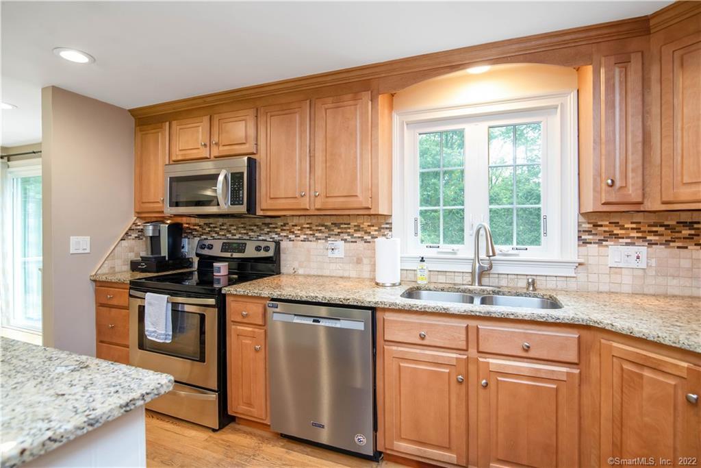 Kitchen with honey-colored cabinets, granite countertops, stainless steel appliances, and a window above the sink.