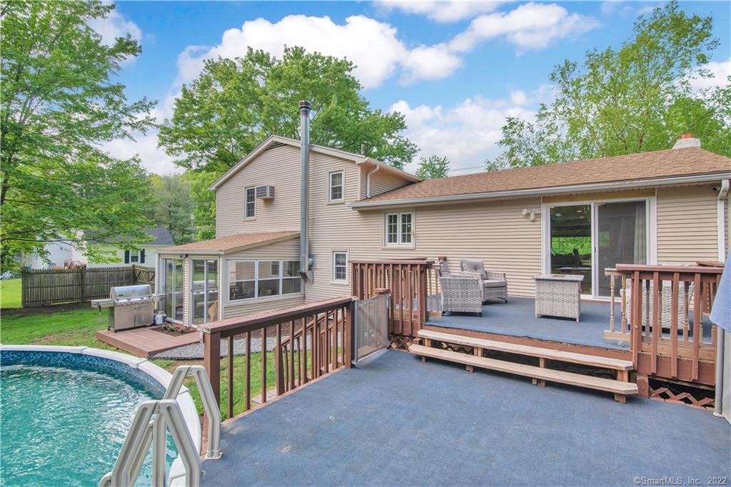 Home’s rear deck overlooks an in-ground pool, with outdoor seating beside sliding glass doors.