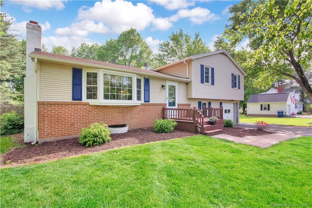 Split-level home with cream siding, brick facade, blue shutters, and a raised wooden entry deck.