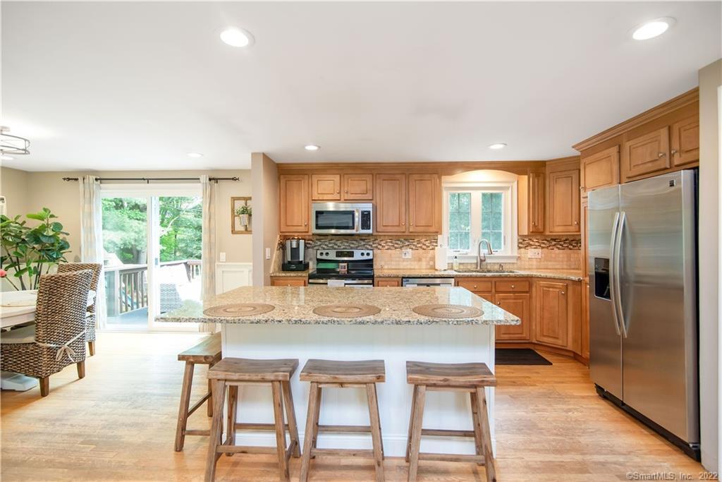 Kitchen with a granite island and three stools, warm wood cabinetry, and stainless steel appliances.