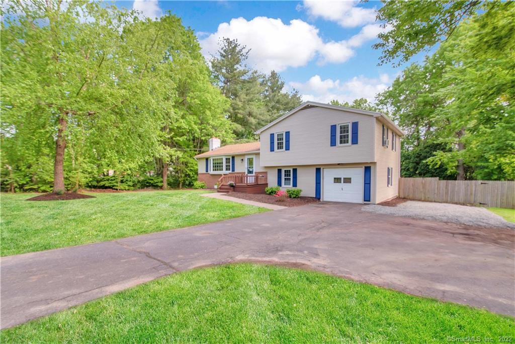 Two-story home with blue shutters and attached garage beside a wide driveway and leafy lawn.