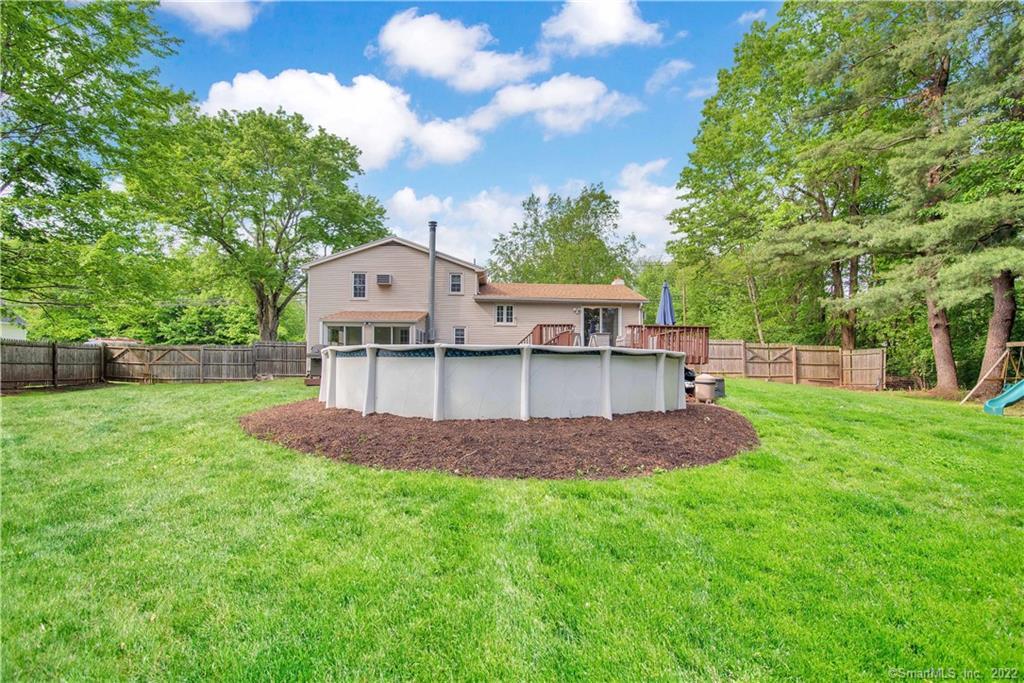 Rear of a beige two-story house with a deck, above-ground pool, and fenced lawn.