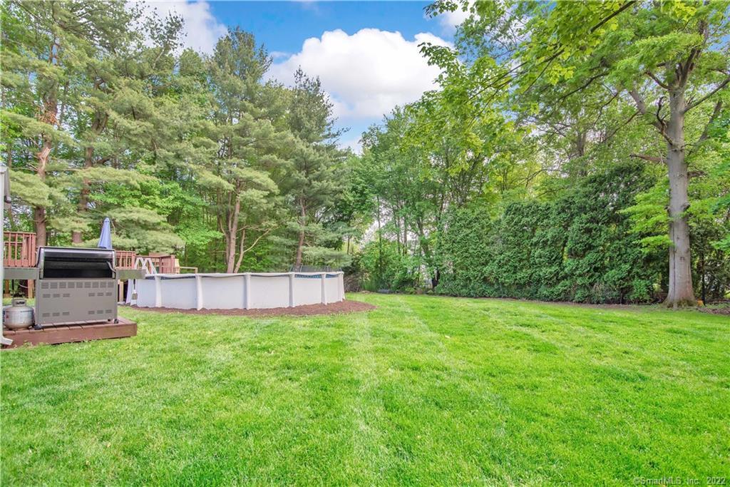 Backyard lawn with an above-ground pool and a deck-side grill, surrounded by mature trees.