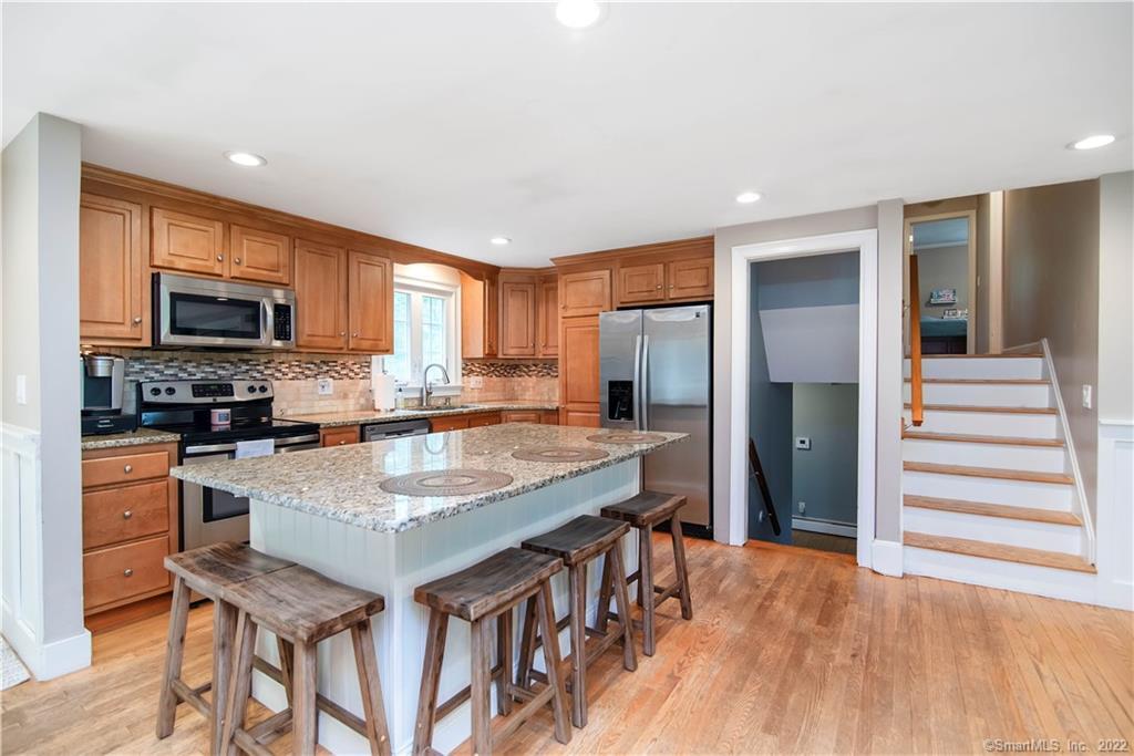 Kitchen with a granite island, wood cabinets, stainless steel appliances, and a staircase.
