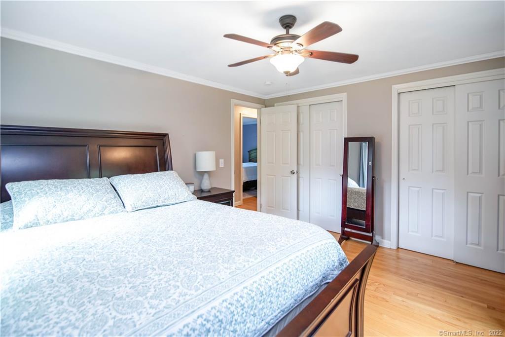 Bedroom with a dark wood bed, patterned white bedding, ceiling fan, and hardwood floors.