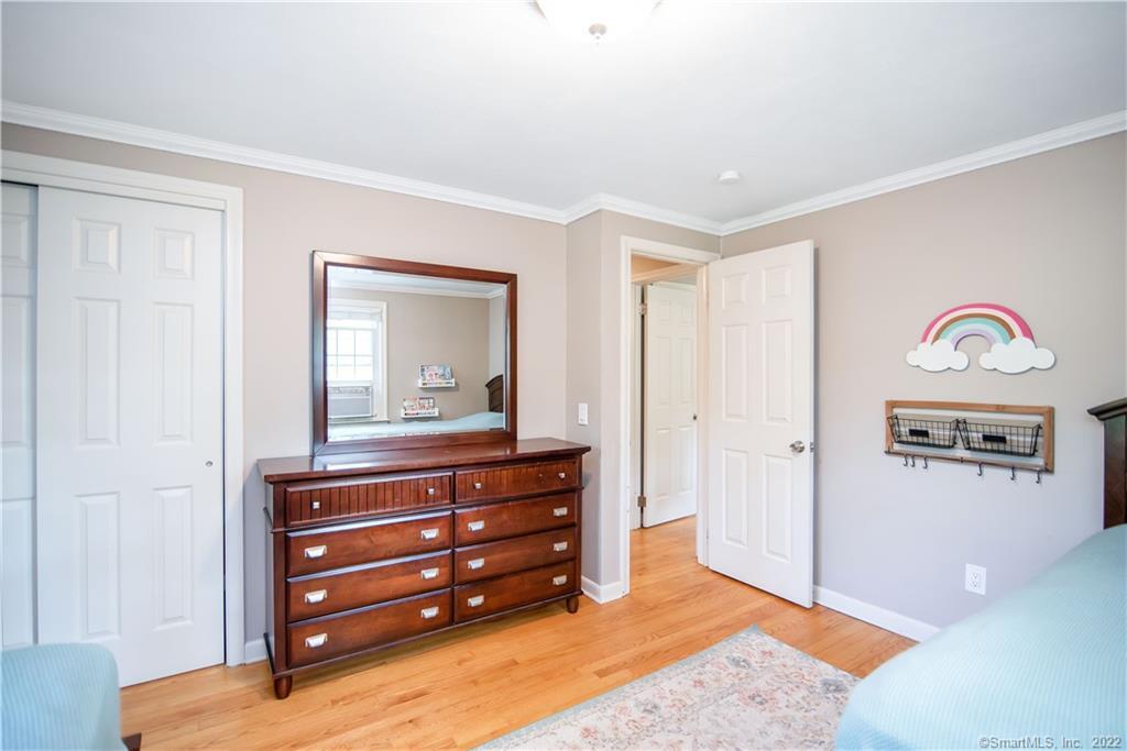 Bedroom with hardwood floors, a dark wood dresser and mirror, and rainbow wall decor.