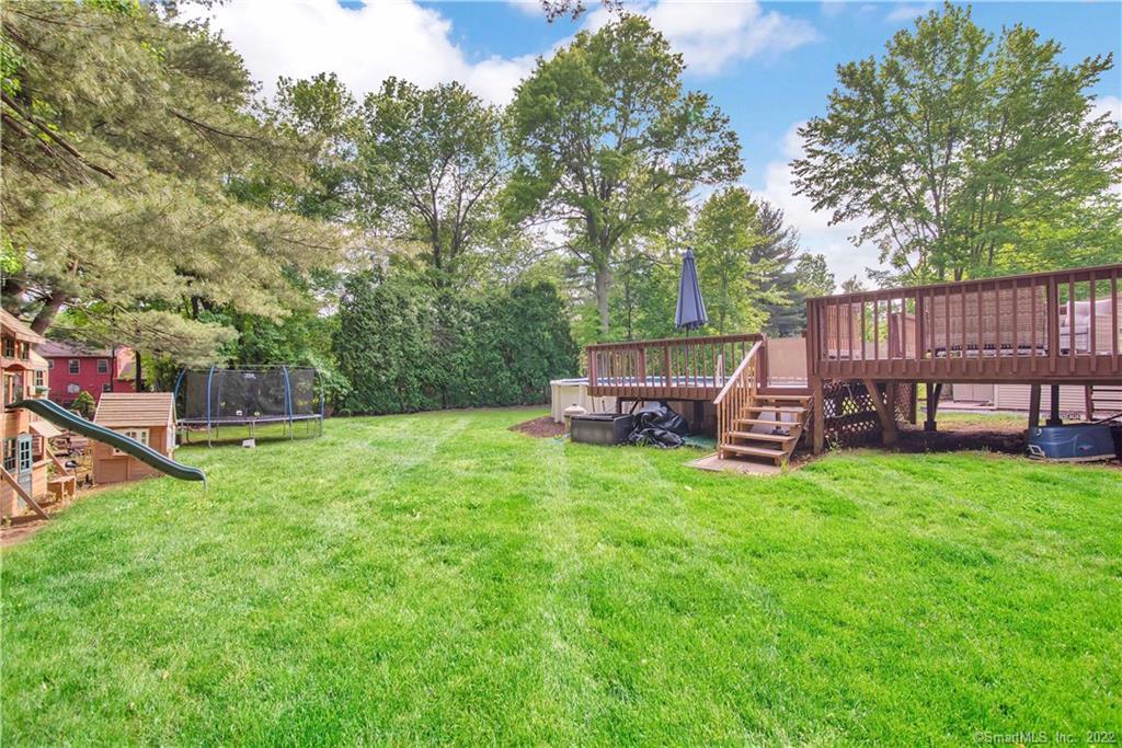Backyard with a wide lawn, raised wooden deck, trampoline, and children’s playset.