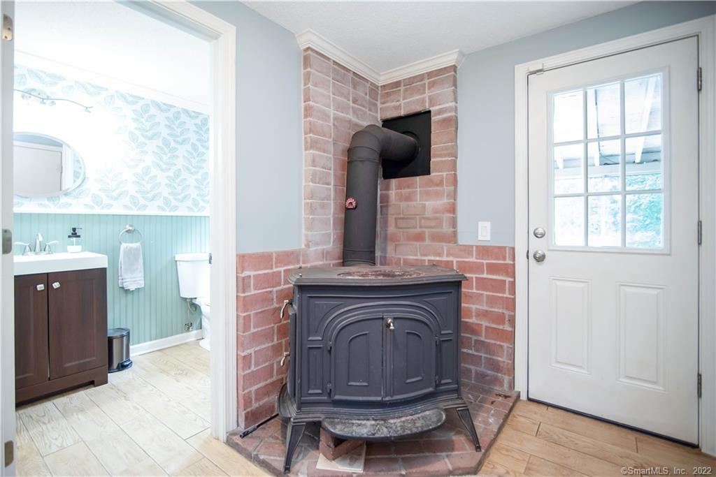 Brick-lined wood stove beside a white exterior door, with an aqua-accented bathroom visible through the doorway.