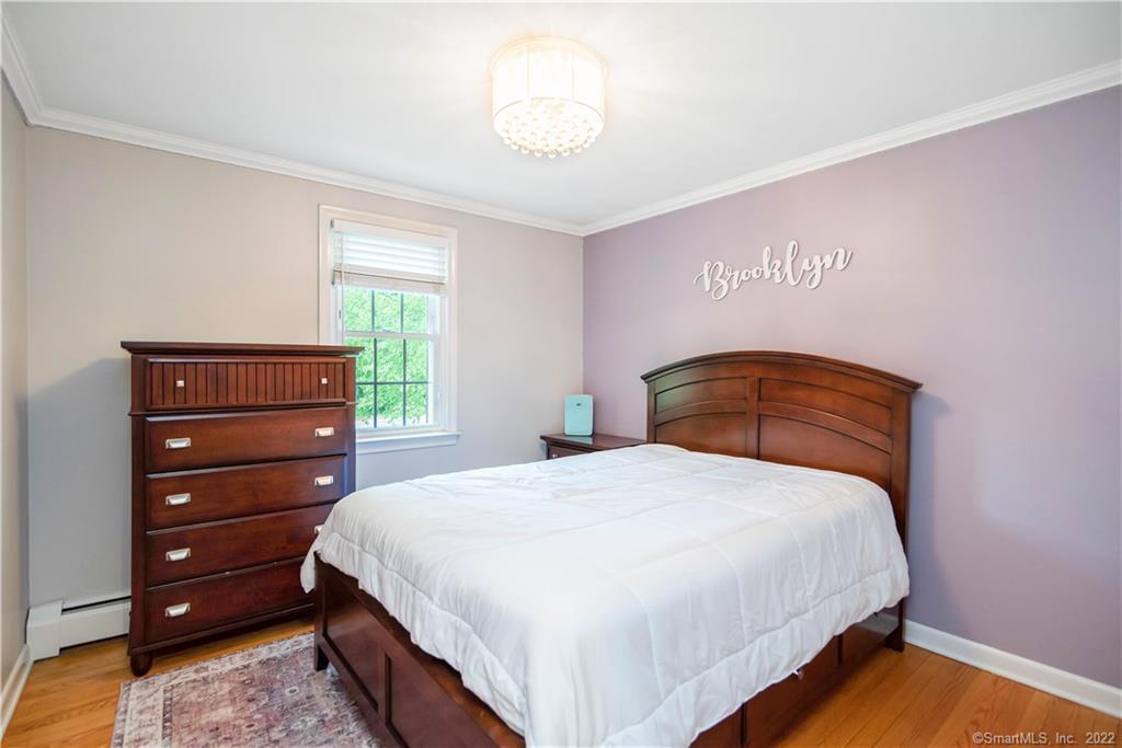 Bedroom with a wooden bed, white bedding, matching dresser, and purple Brooklyn accent wall.