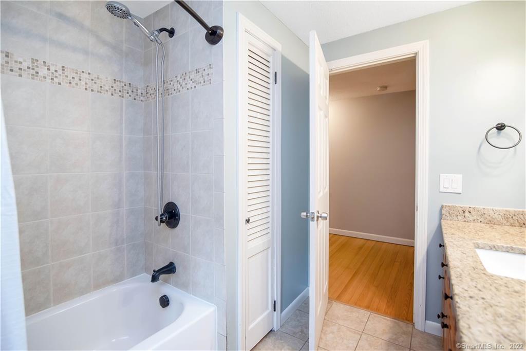 Bathroom with tiled tub and shower, mosaic accent band, and granite vanity.