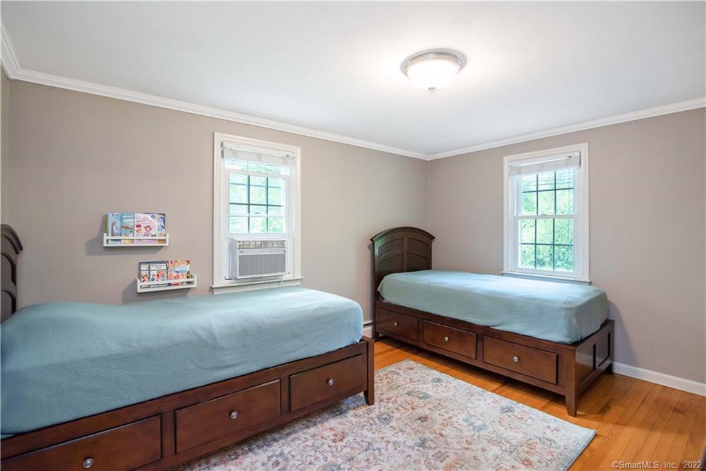 Bedroom with two wooden beds, blue bedding, windows, and hardwood floors.