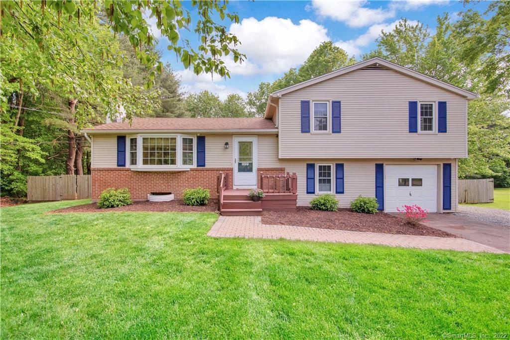 Split-level home with a brick lower facade, blue shutters, attached garage, and broad green lawn.
