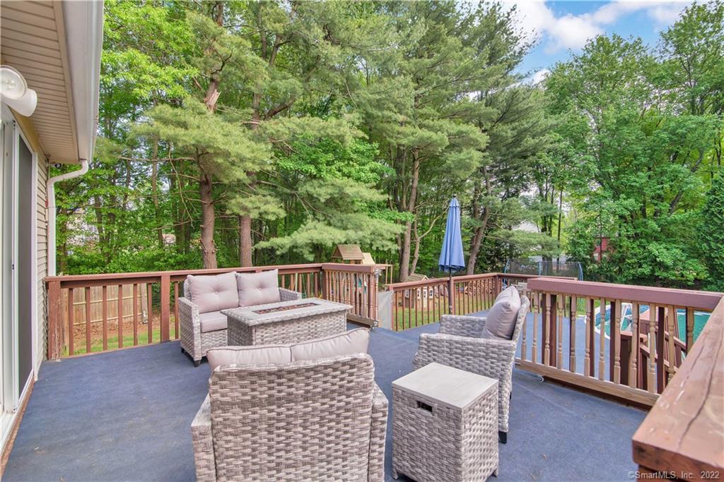 Deck with wicker patio furniture and a blue umbrella, overlooking a leafy wooded backyard.