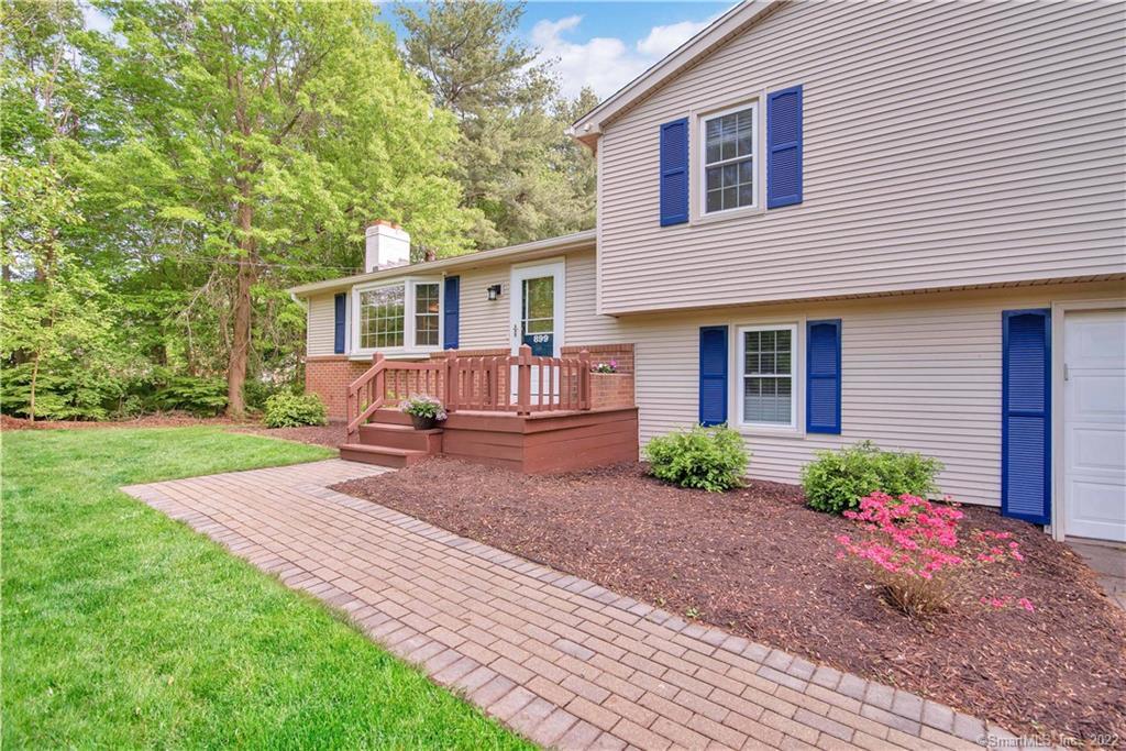 Beige split-level home with blue shutters, raised entry deck, and brick walkway.