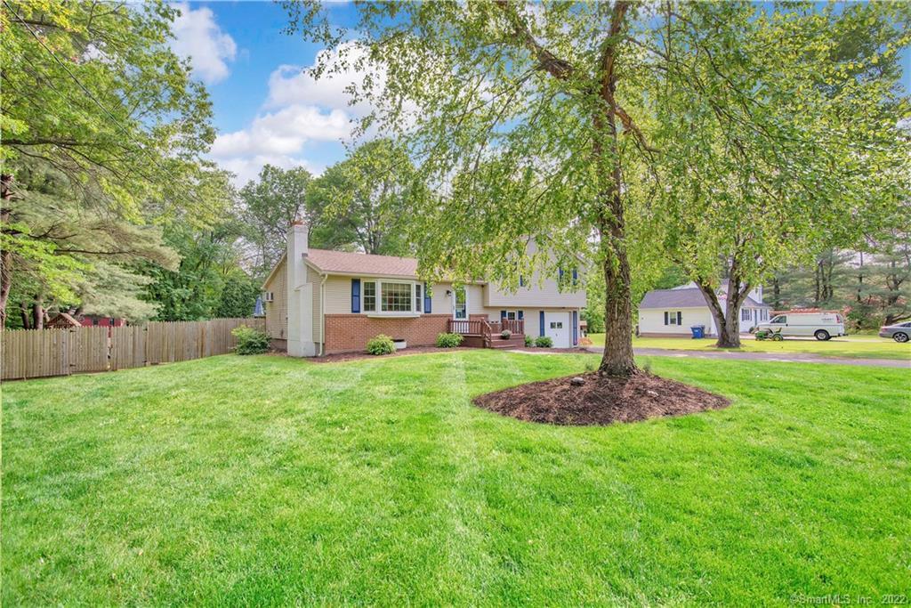 Split-level home with brick facade, blue shutters, and a broad lawn beneath mature trees.