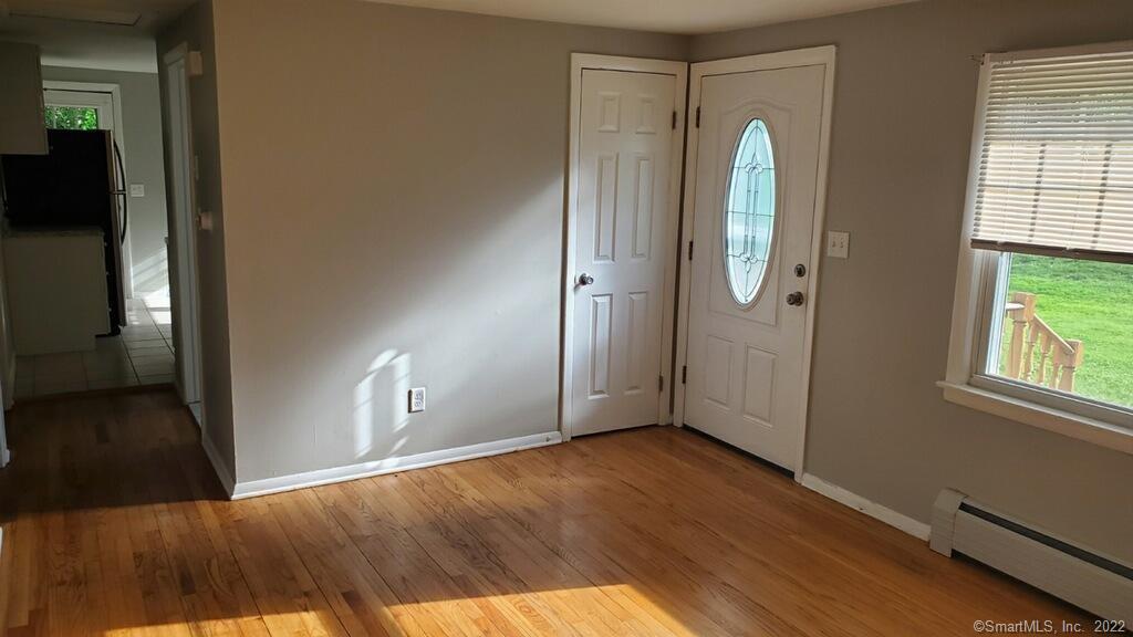 Vacant room with hardwood floors, a glass-panel entry door, and a window overlooking the lawn.