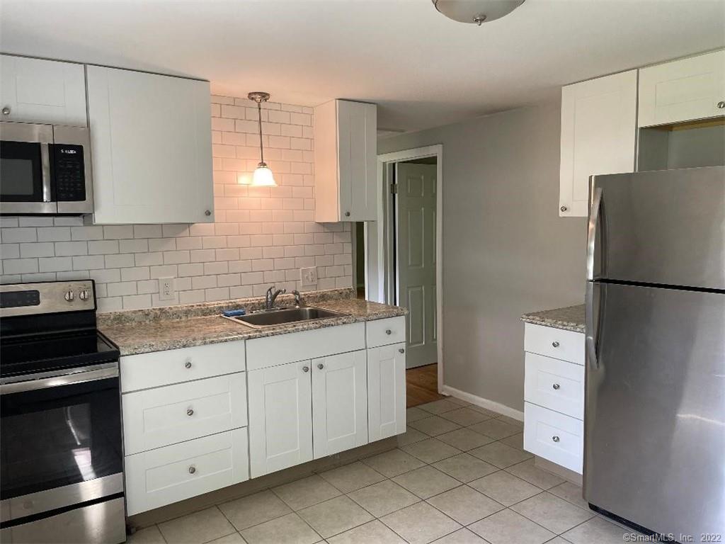 Kitchen with white cabinets, granite countertops, subway-tile backsplash, and stainless-steel refrigerator.