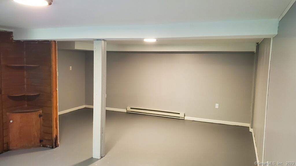 Empty finished basement with gray floors, a support post, and built-in wooden shelving.
