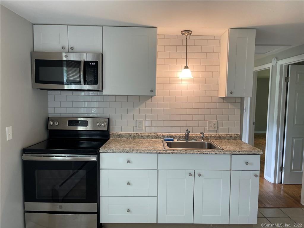 Kitchen with white cabinets, subway tile backsplash, granite counters, and black range.