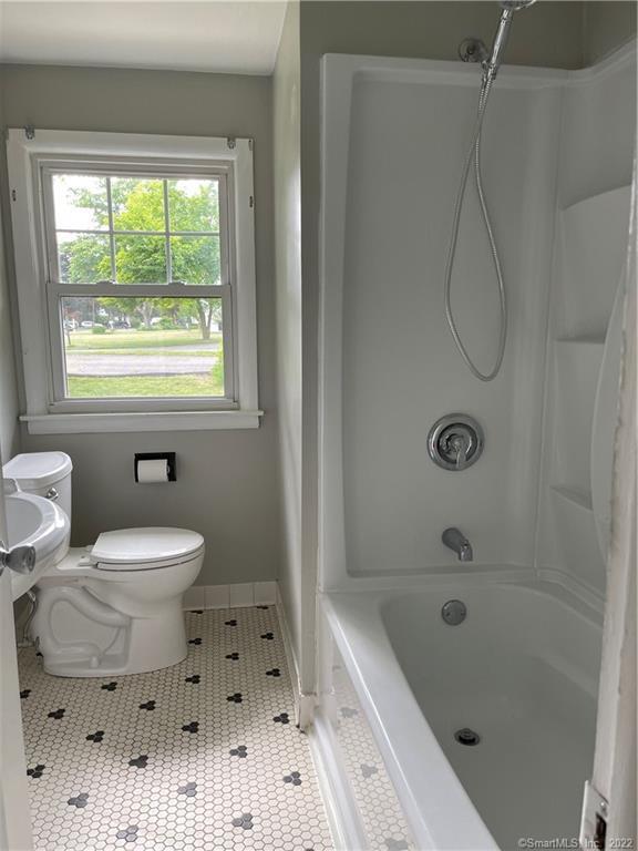 Bathroom with a white tub and shower, hexagonal tile floor, and a window overlooking the street.