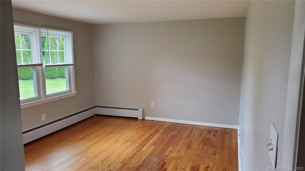 Empty room with hardwood floors, two windows, and baseboard heating.