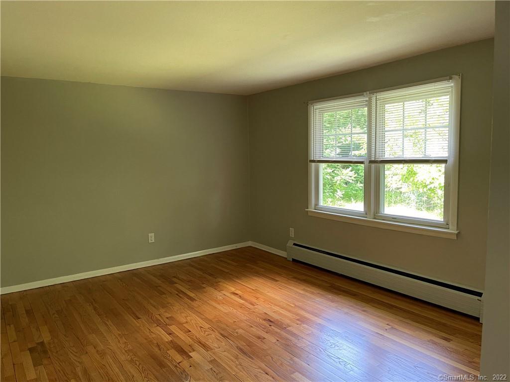 Empty bedroom with hardwood floors, olive-green walls, and two windows with blinds.