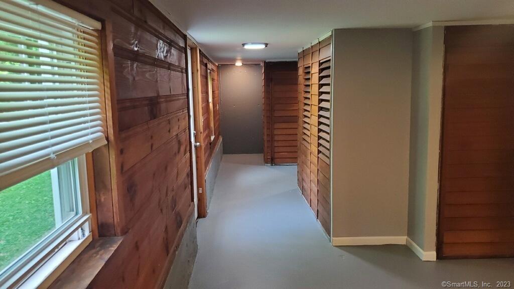 Hallway with wood-paneled walls, carpet, a window with blinds, and louvered closet doors.