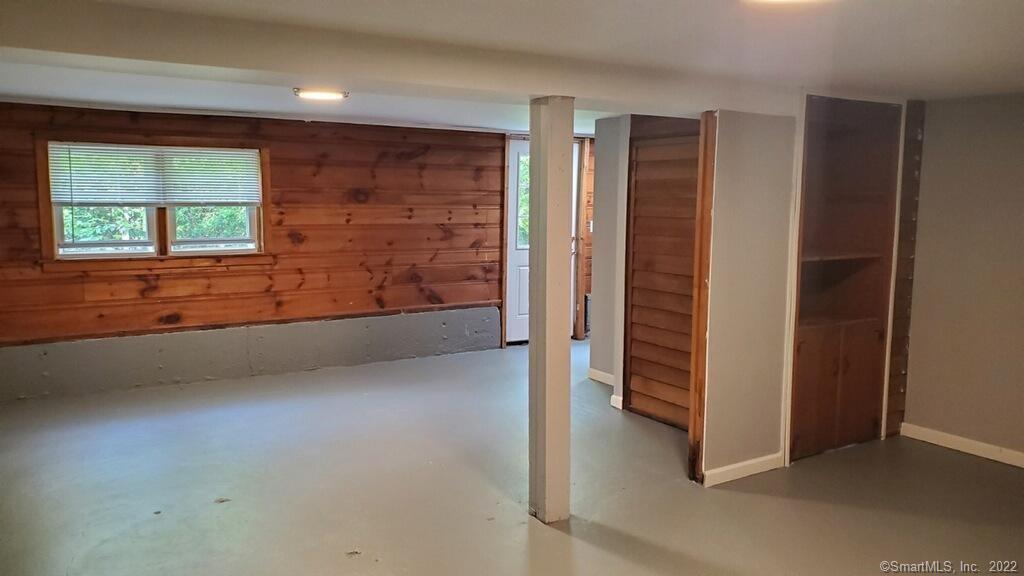 Empty basement room with wood-paneled walls, small windows, and built-in storage.