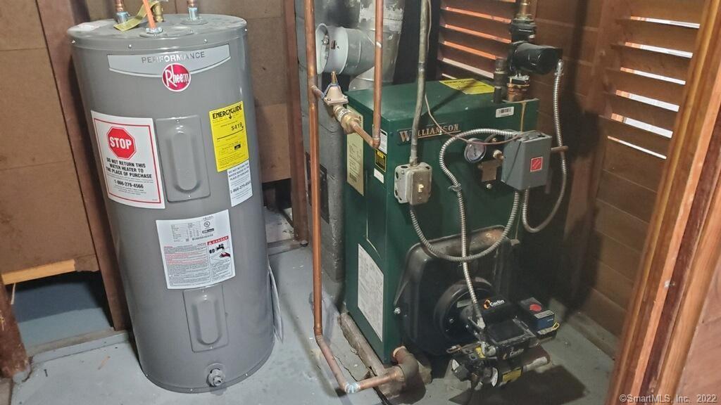 Utility room with a Rheem water heater beside a green boiler and exposed pipes.
