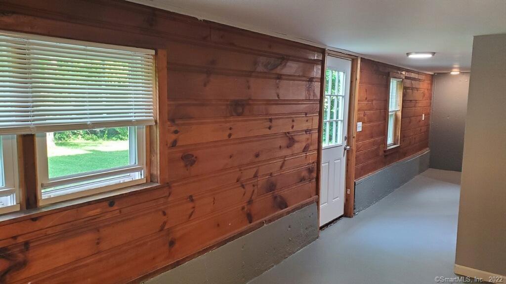 Hallway with knotty wood walls, window blinds, and a white exterior door.
