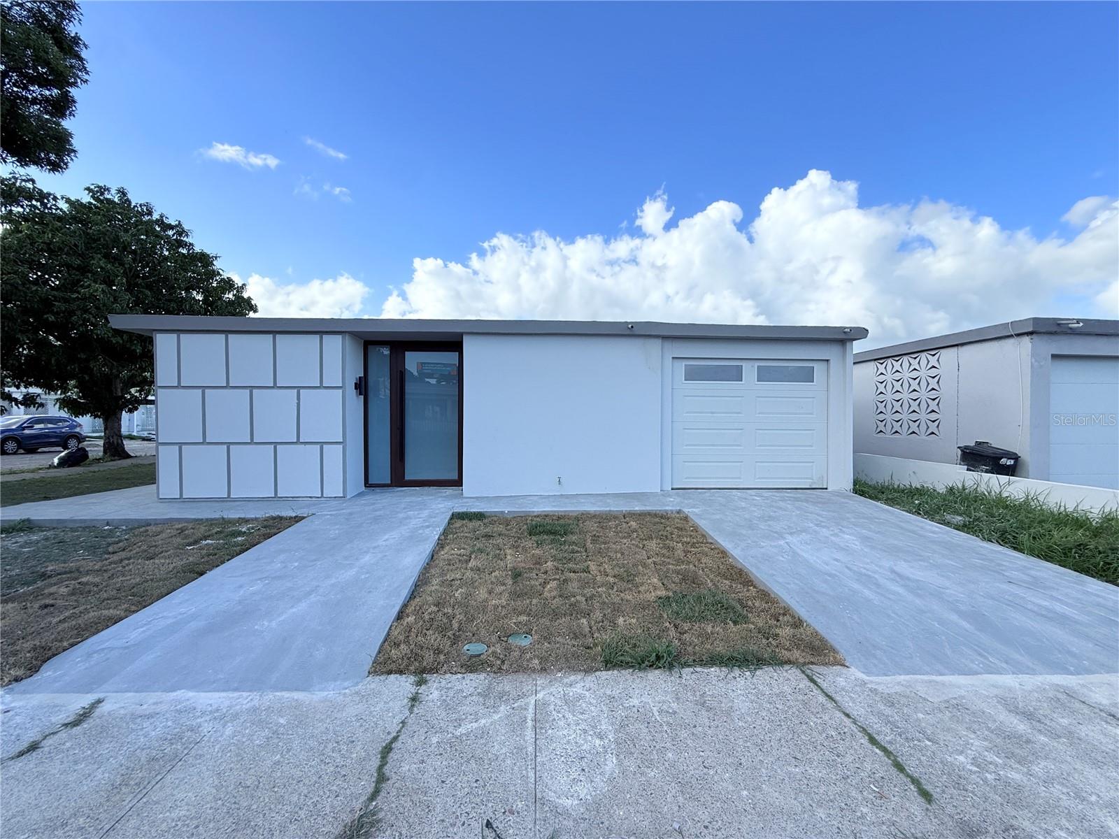 Modern single-story white home with a dark-framed entrance, garage, and concrete driveway.