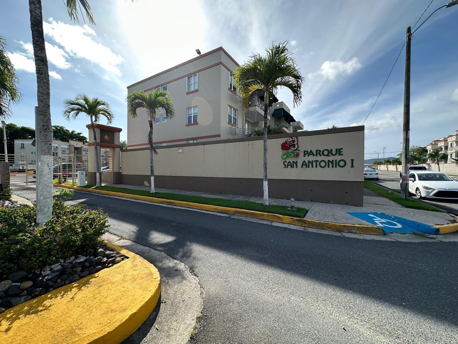 Parque San Antonio I condominium entrance with its name on the wall and palm trees in front.