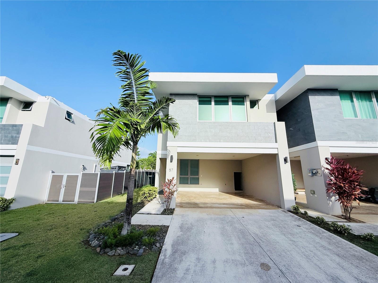 Modern two-story white and gray home with a covered driveway and palm tree.