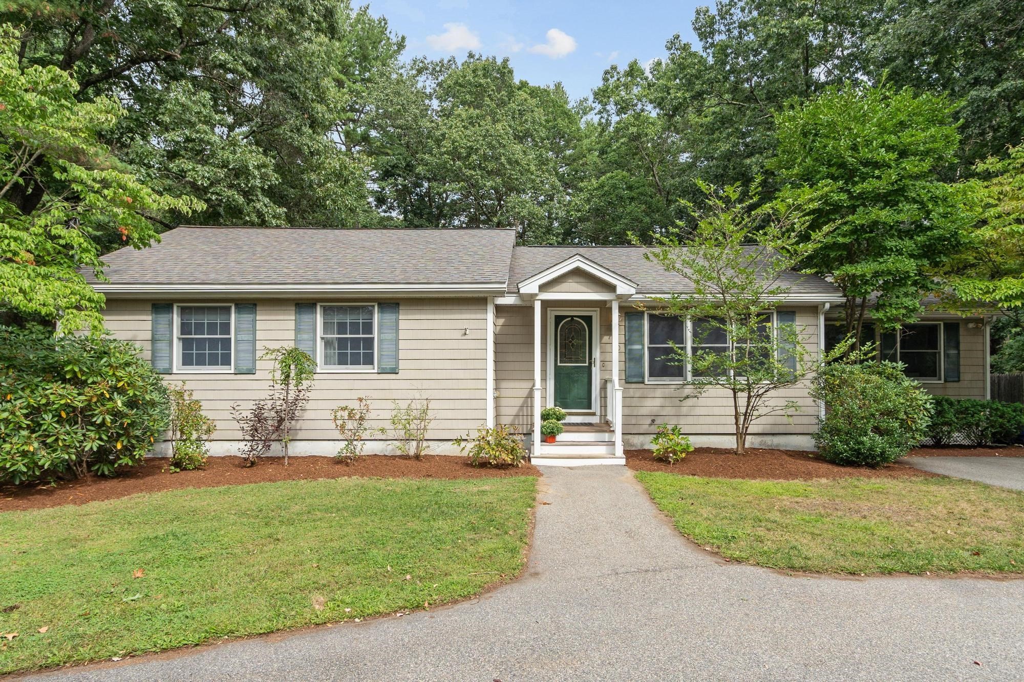 Single-story beige house with a green front door, white entry steps, and mature trees.