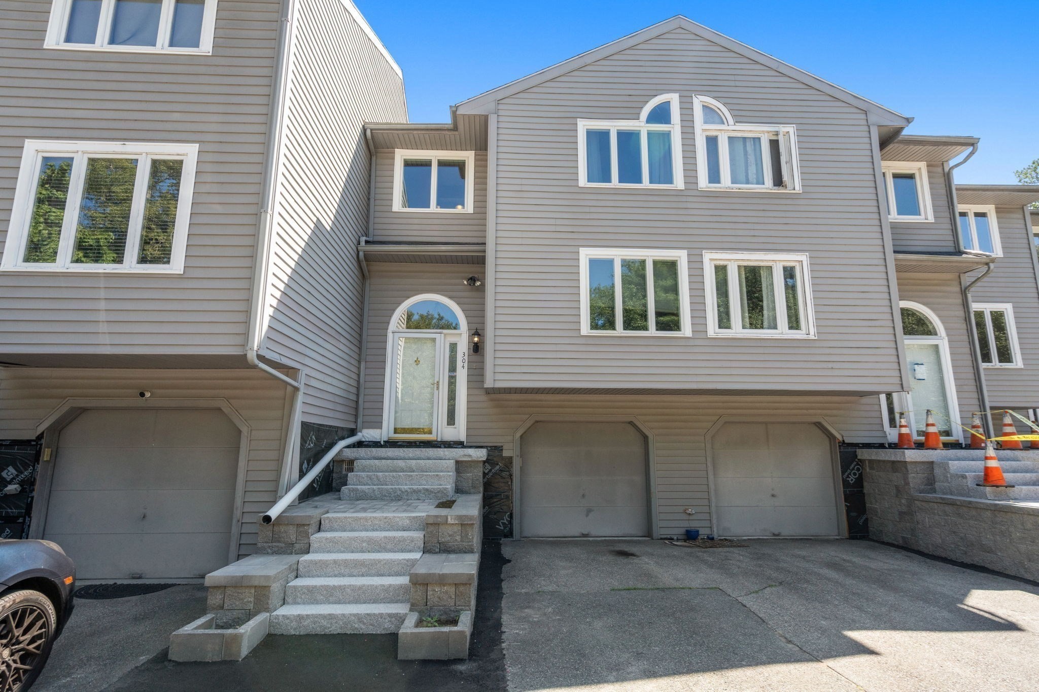 Gray-sided multi-unit home with stone entry steps, garage doors, and construction cones.