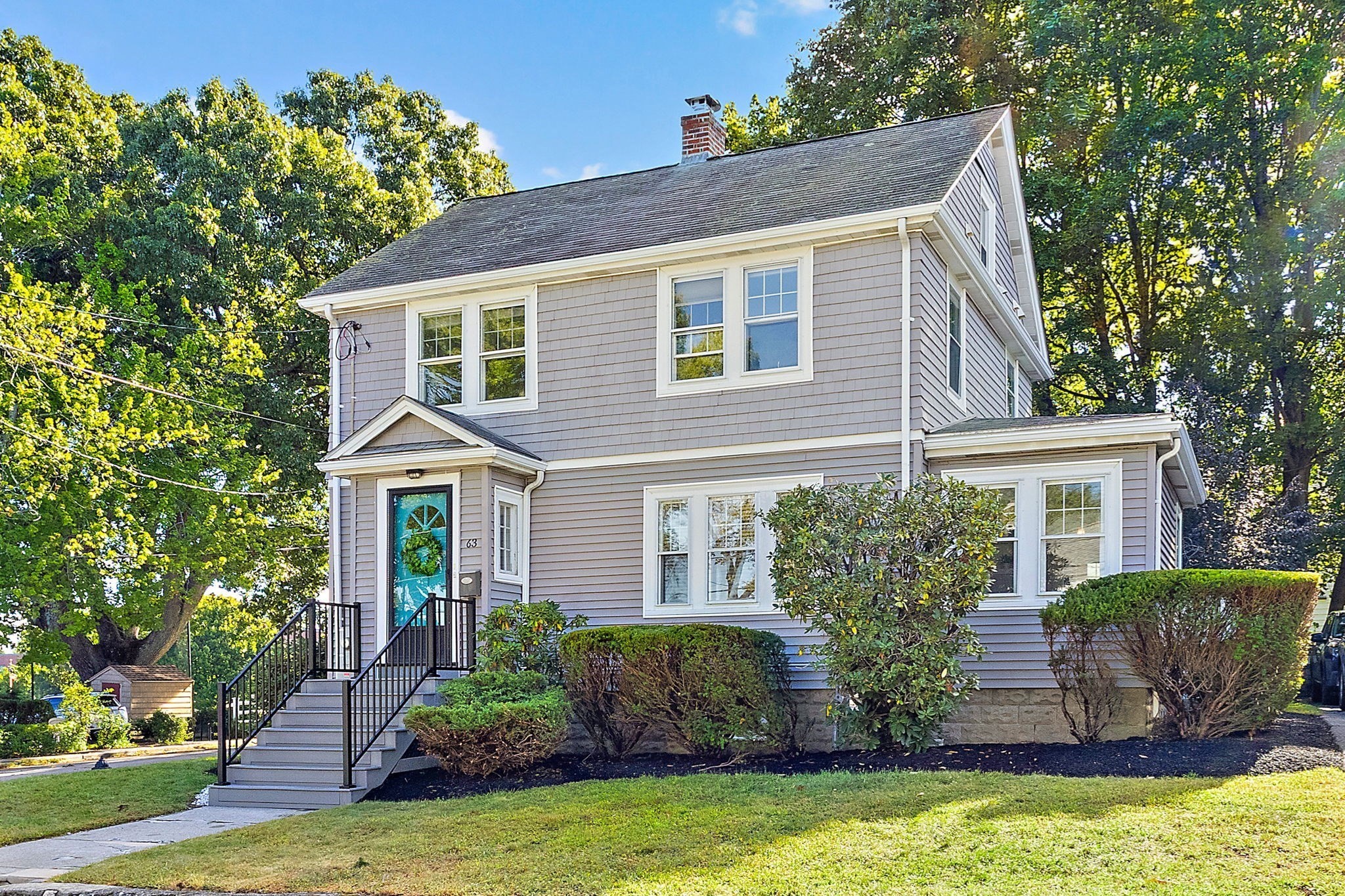 Gray two-story house with white trim, turquoise front door, and black entry stairs.