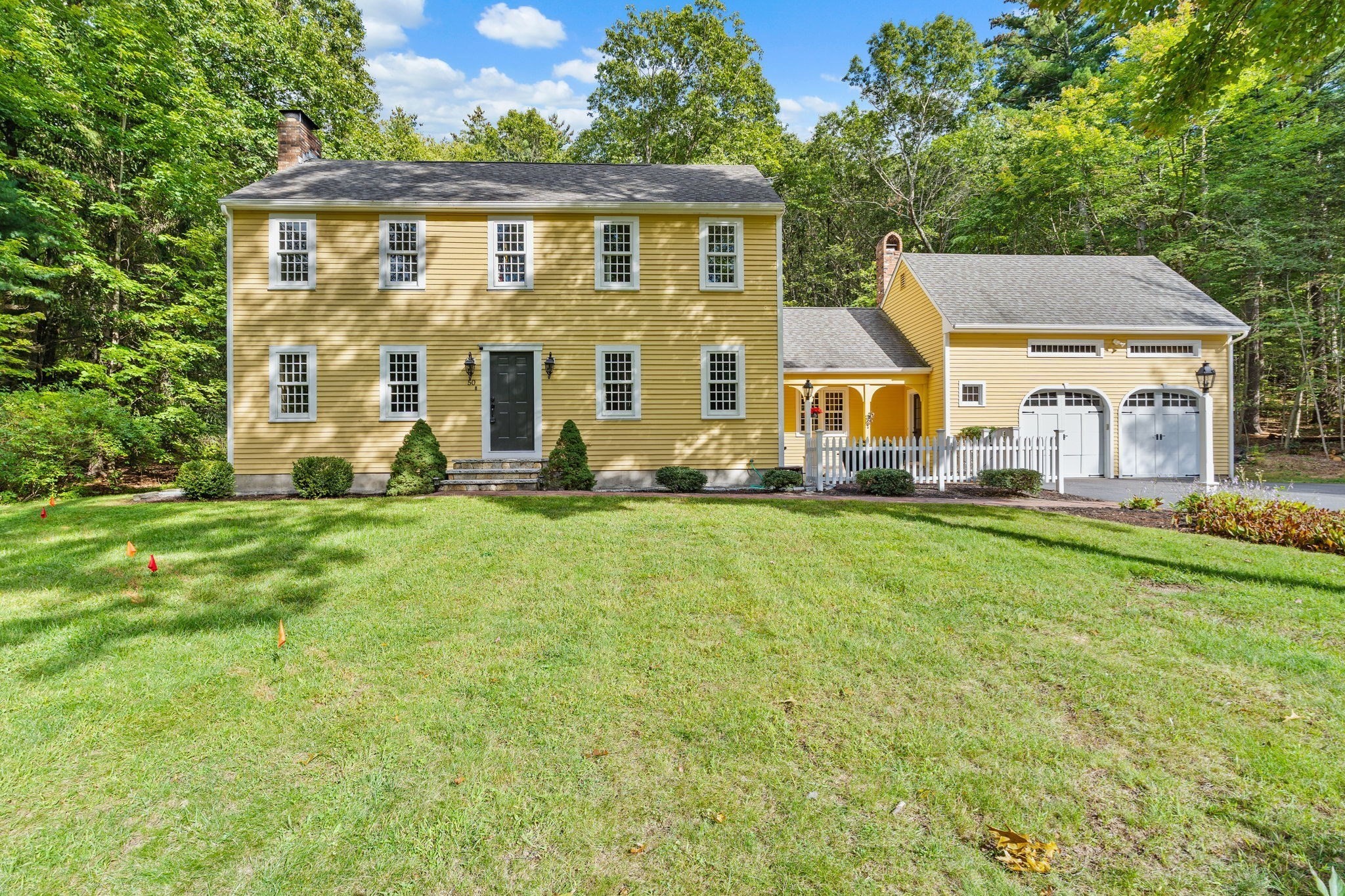 Yellow colonial home with attached double garage, white picket fence, and a broad front lawn.