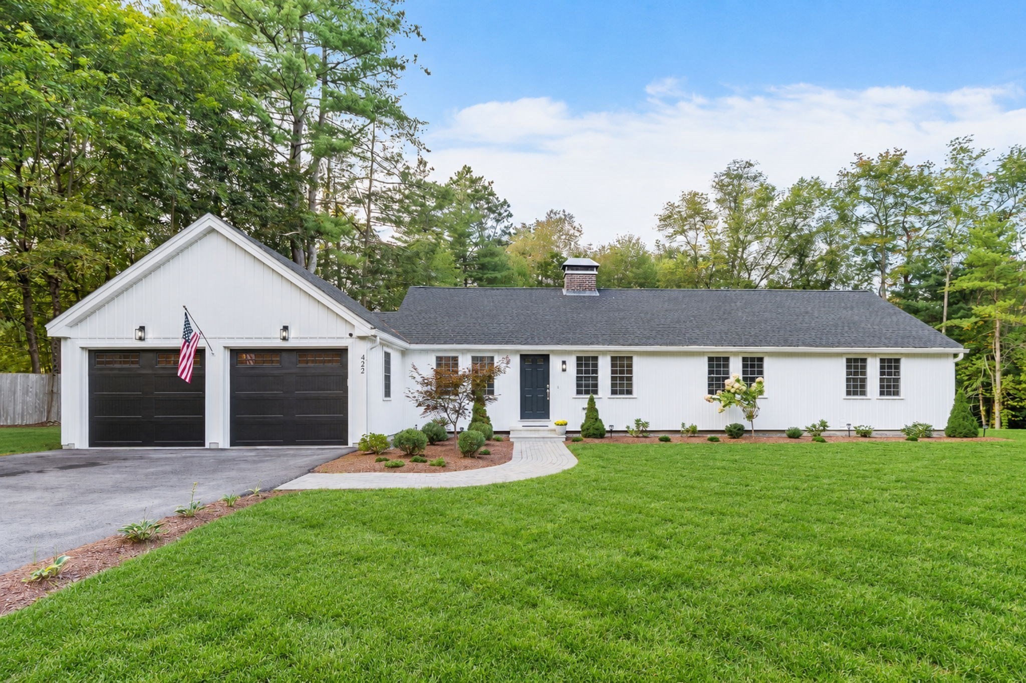 White single-story home with twin black garage doors, an American flag, and a landscaped front lawn.