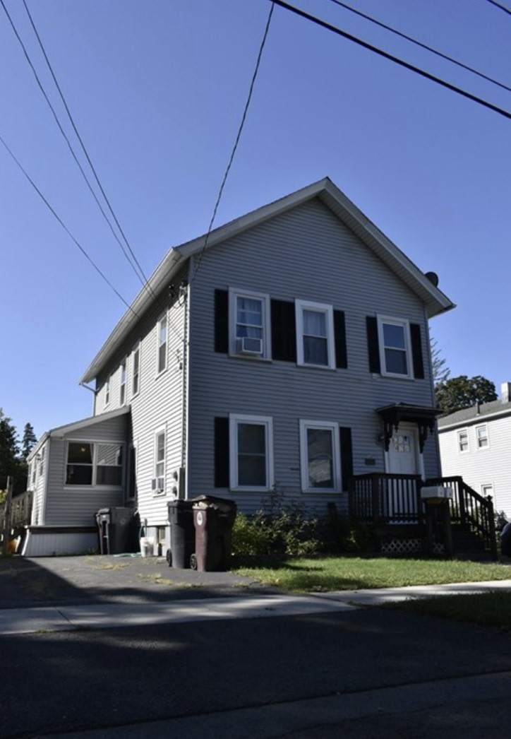 Two-story gray house with black shutters, a side addition, and a small front porch.