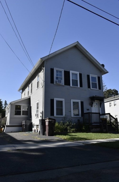 Two-story gray house with black shutters, a small front porch, and a driveway.