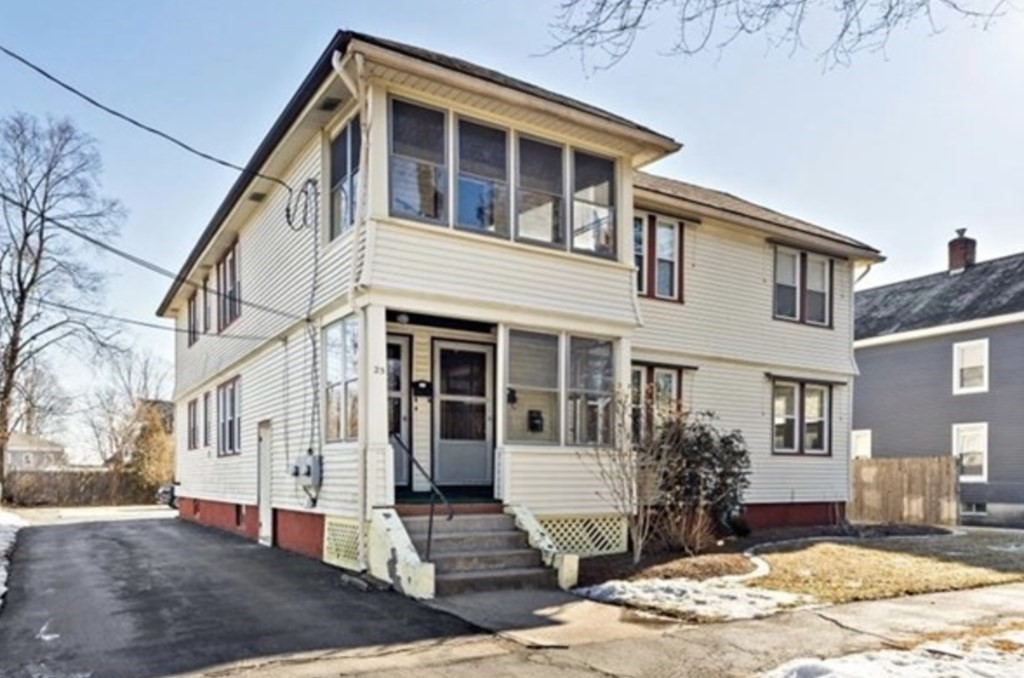 Cream two-story house with an enclosed upper porch, front steps, and a paved driveway.