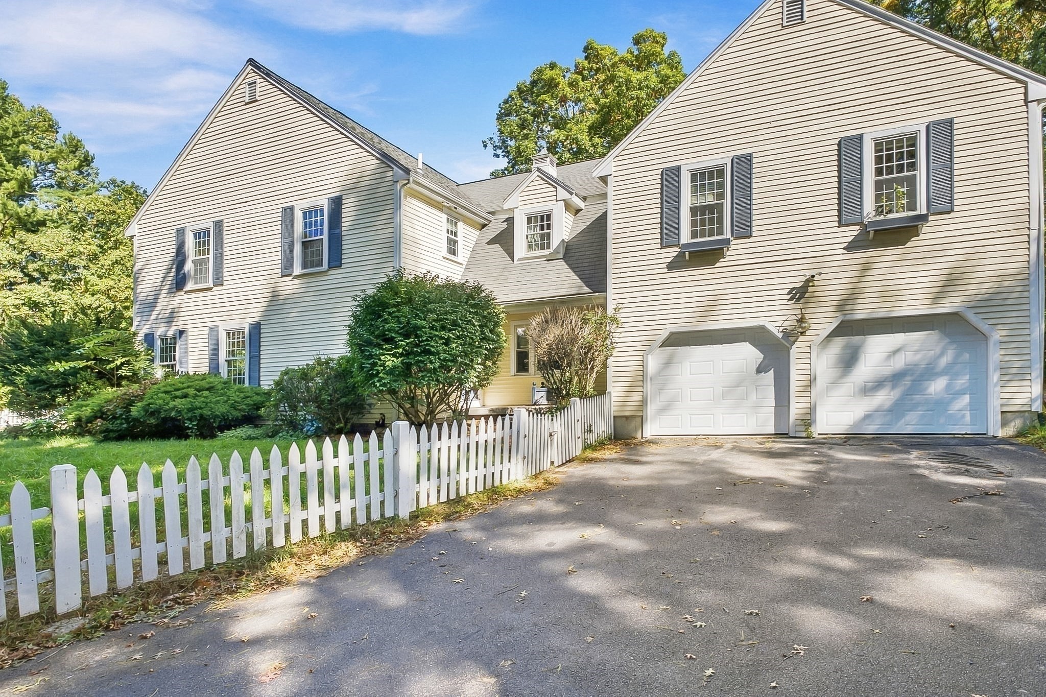 Two-story house with blue shutters, twin garage doors, and a white picket fence.