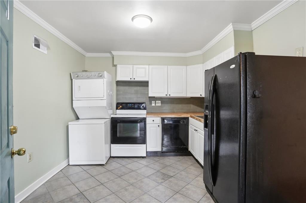 Kitchen with white cabinets, stacked washer and dryer, white range, and large black refrigerator.