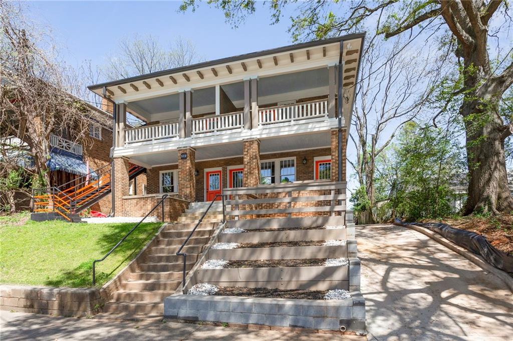 Two-story brick home with covered porches, red doors, and a broad central staircase.