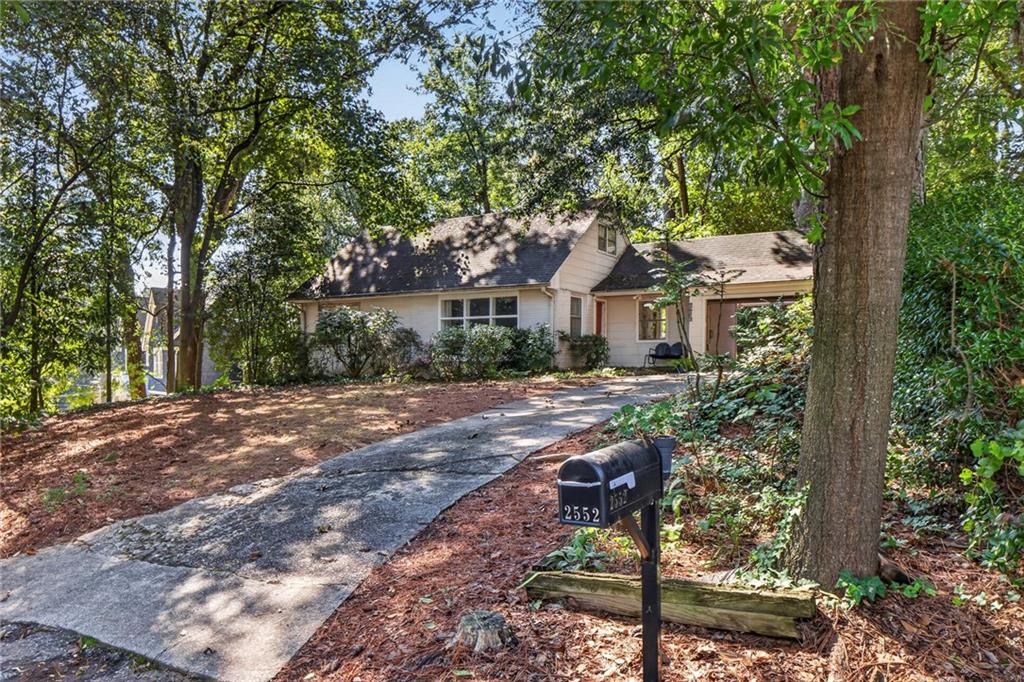 Light-colored home among mature trees, viewed from the driveway beside mailbox 2552.